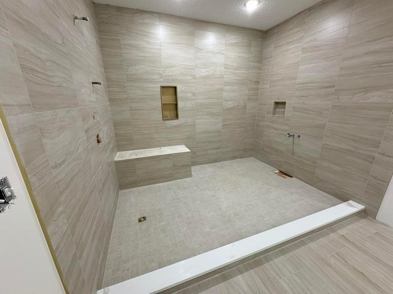 Large custom walk-in shower with bench, double shower heads, and large format tile
